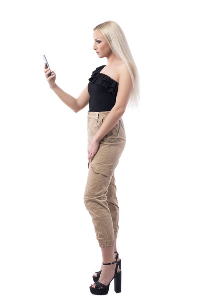 Zijaanzicht van vrouwelijke mooie blonde haar vrouw surfen op Internet op smartphone. Volledige lichaam geïsoleerd op witte achtergrond.  - Foto, afbeelding
