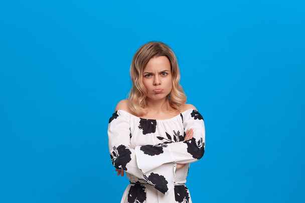Angry blonde young woman in a white dress standing over blue background - Photo, Image