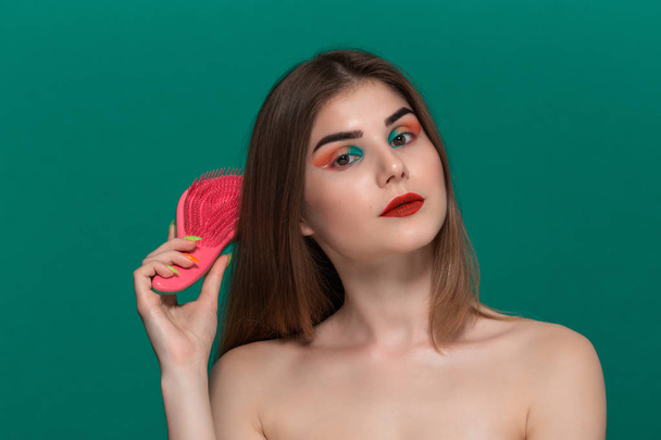 Portret van mooie jonge vrouw met felle kleuren make-up kammen haar met een borstel - Foto, afbeelding