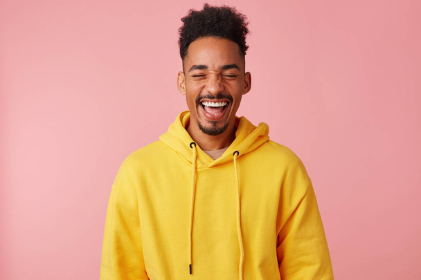 Νέος χαρούμενος χαμογελαστός Αφρικανός Αμερικανός τύπος με κίτρινη κουκούλα, άκουσε - Φωτογραφία, εικόνα