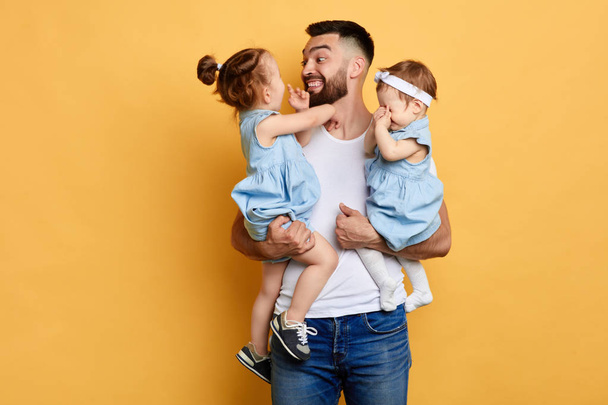 Young happy father with his little daughters on yellow background - 写真・画像