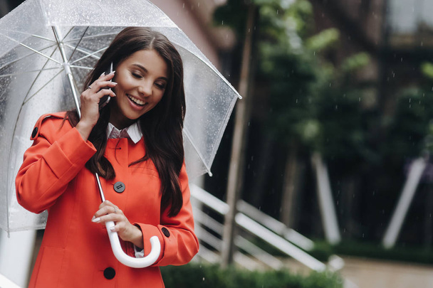 Brunette woman talking on phone holding umbrella, it rains. Outdoor portrait of young woman talking with friend on mobile phone - Foto, immagini