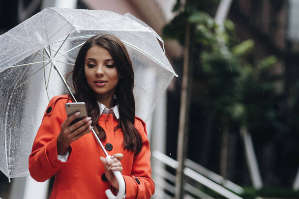 Business woman holding umbrella and texting from her cell phone near the office. - Foto, afbeelding