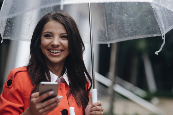 Portrait of beautiful smiling woman with transparent umbrella writing message in city. - Φωτογραφία, εικόνα