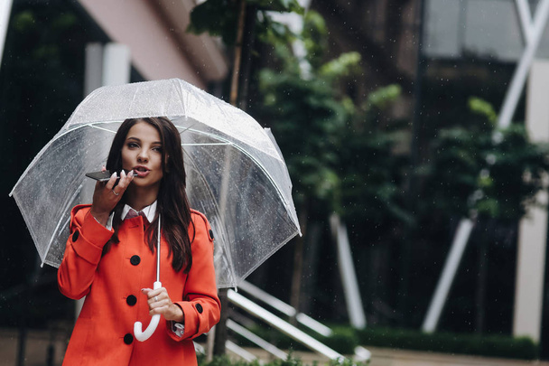 Businesswoman in red with transparent umbrella calling on smartphone on the street. - Foto, Bild