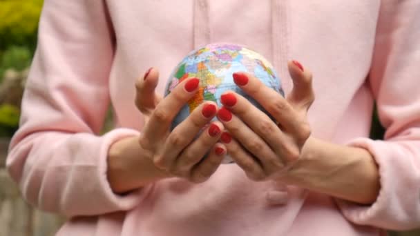 Female hands with red manicure giving a small globe with geografical names in Ukrainian cyrillic letters on it. Ecological problems concept - 映像、動画