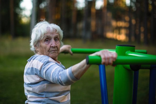 Vanha nainen tekee liikuntaa kadulla urheilu leikkipaikka
. - Valokuva, kuva