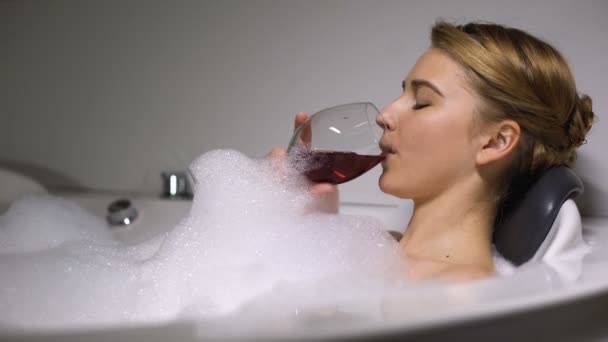 Happy woman drinking wine in bath with foam bubbles, relaxing after hard workday - Footage, Video