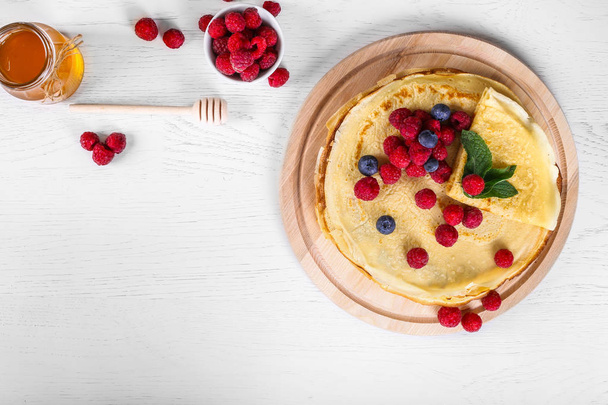 Top view of pancakes with raspberries and blueberries. Healthy summer breakfast,homemade classic russian pancakes, morning light background, copy space, top view. Stack of russian thin pancakes blini - Foto, afbeelding