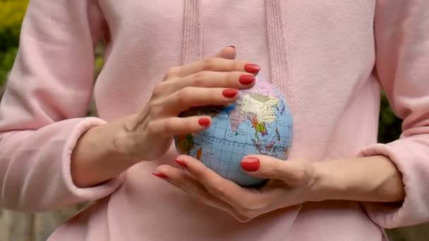 Eine junge Teenagerin in pinkfarbener Freizeitkleidung mit roter Maniküre hält in ihren Händen eine kleine Weltkugel mit geografischen Namen in ukrainischen kyrillischen Buchstaben. Umweltverantwortungskonzept. - Filmmaterial, Video