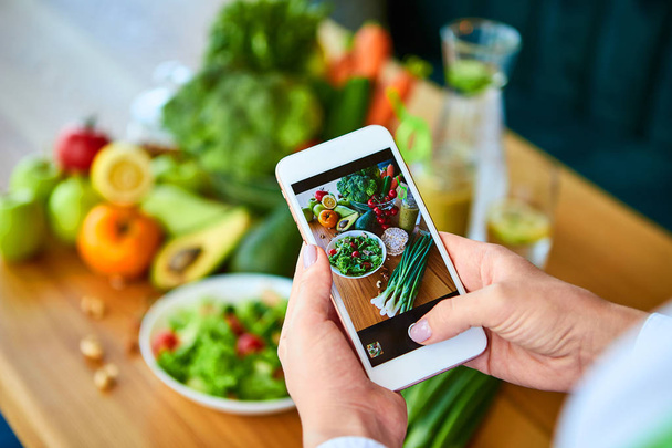 Vrouw handen nemen smartphone voedsel foto van groenten Salade met tomaten en fruit. Telefonische fotografie voor sociale media of bloggen. Veganistische lunch, vegetarisch diner, gezond dieet  - Foto, afbeelding