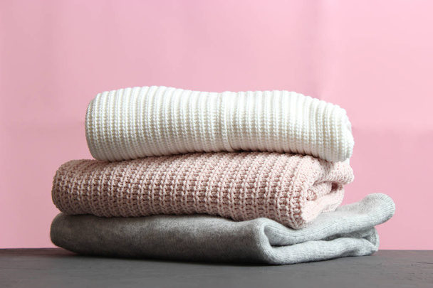 A pile of warm sweaters on a wooden table on a color background. Autumn and winter clothes. - Foto, afbeelding
