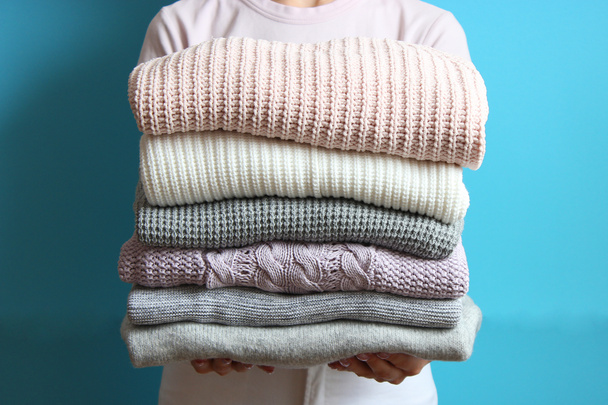 стопка свитеров в женских руках на цветном фоне - Фото, изображение