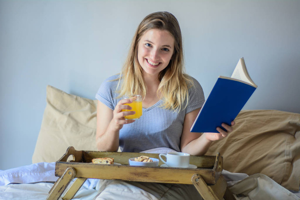 Woman reading a book and having breakfast. - Фото, изображение