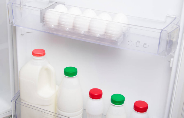 close-up, on the shelf in the door of the white refrigerator, dairy products, kefir, cream and eggs - Фото, изображение
