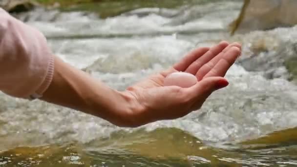 川の背景にバラの水晶ヨニ卵を保持している女性の手。女性の健康、自然の概念との一体性. - 映像、動画