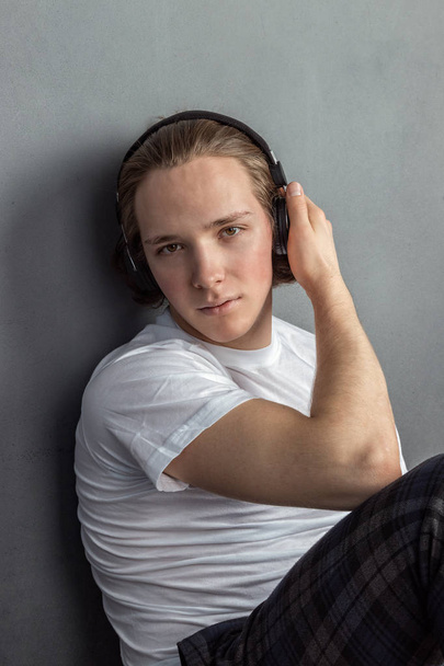 Handsome young man sitting on the floor in living room, having headphones on his head and listening music - Photo, Image