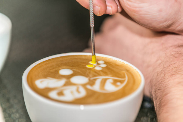 Barista making an art from the fresh milk in the little ceramic cup of the delicious hot espresso - Photo, Image