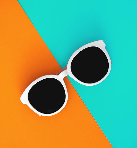 Sunny stylish white sunglasses on a bright blue-cyan and yellow-orange background, top view, isolated. Copy space. Flat lay - Foto, Bild