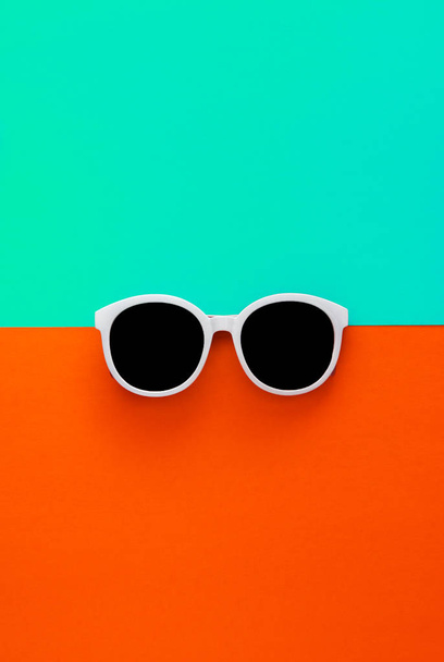 Zonnige stijlvolle witte zonnebril op een heldere blauw-cyaan en rood-oranje achtergrond, bovenaanzicht, geïsoleerd. Kopieer ruimte. Platte lay - Foto, afbeelding