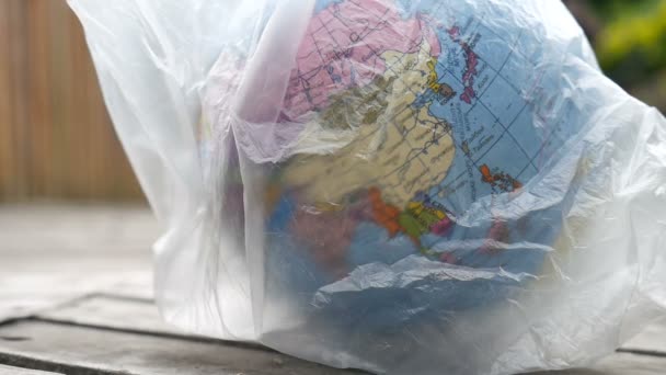 Side view of the globe of Earth in polyethylene disposable package on wooden background. Concept of ecological problems. Stop garbage pollution - Footage, Video