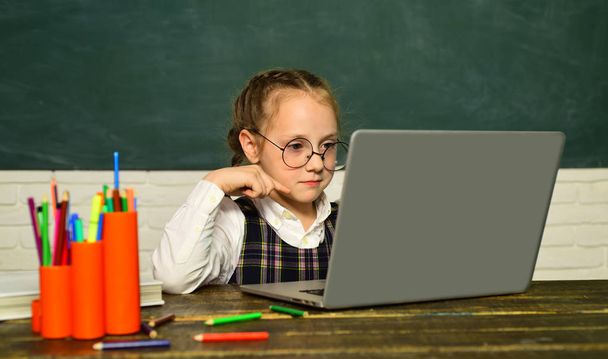 Pupil working on laptop computer over blackboard background. School kids. Teachers day. Funny little child having fun on blackboard background. - 写真・画像