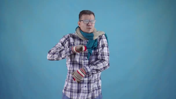 Distressed frozen man covered with frost in gloves and scarf on blue background shows finger down - Кадры, видео