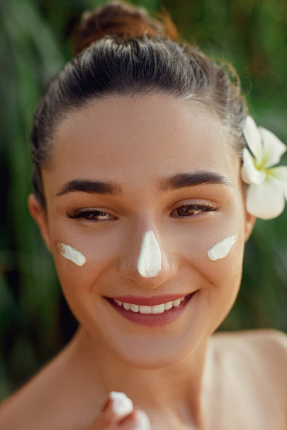 Beautiful Young woman with moisturizing  cream on face. Girl holding bottle   cosmetic cream. Female applying  lotion on skin. Skin care. Sun protection. - Fotó, kép