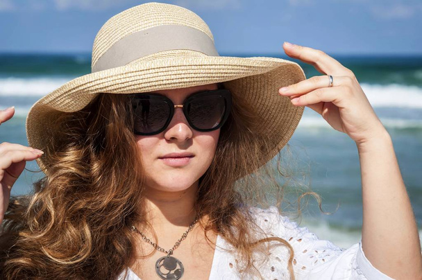 Mladá elegantní Kavkazská dáma v slaměném klobouku s slunečními brýlemi u moře. Ochrana před obrázkem sluneční koncepce. - Fotografie, Obrázek