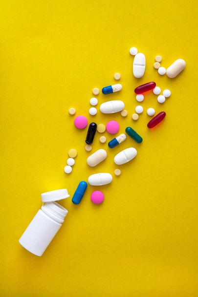A variety of medicinal pills and pills poured out of the vial on a yellow background. Flat lay. Copy space. Trend. The concept of a healthy, bright, modern medicine and pharmacology - Fotoğraf, Görsel