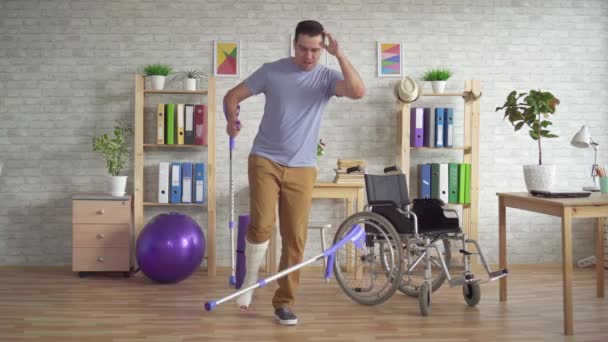 Vrolijke expressieve man met een gebroken verbonden been speelt krukken als een gitaar - Video