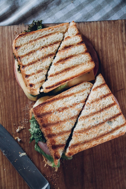 Dva sendviče na dřevěném pozadí, pohled shora. Hromádka Panini se šunkou, sýrem a salátem na střihací desce - Fotografie, Obrázek