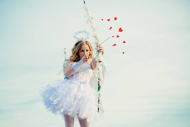 Little goddess with white wings alone on blue sky background. Portrait of little curly blond Angel girl. Girl angel with halo in white angel dress. Enjoying magic moment - Photo, image