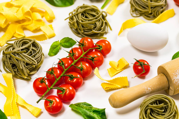 Spinach and Basil Pasta Nests, Ribbon Pasta Noodles with Tomatoes and Ingredients for Cooking Pasta on White Wooden Background, Italian cuisine, Top view. Selective focus. - Photo, Image