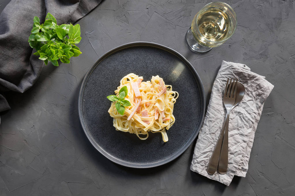 Pasta tagliatelle with bacon and wine glass on black background. Delicious Mediterranean lunch. - Фото, изображение