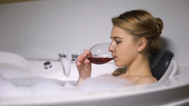 Depressed girl lying in bath with foam bubbles drinking wine, boyfriend break up - Кадры, видео