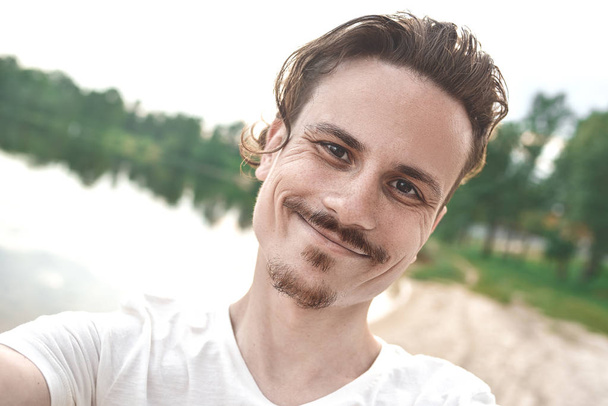 Bonito sorriso caucasiano cara tira uma selfie na praia - pessoas, estilo de vida. olhando para a câmera
 - Foto, Imagem