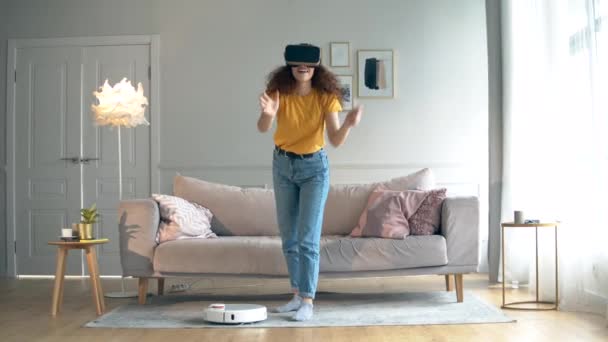 Girl uses VR headset while a robotic vacuum cleaner works. - Imágenes, Vídeo