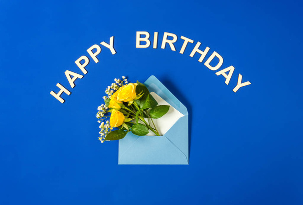 Sarı güller ve beyaz Gypsophila mavi zarfta mavi arka planda yakın çekim. Metin mutlu Doğum günü. Üst görünüm, düz yatıyordu. - Fotoğraf, Görsel