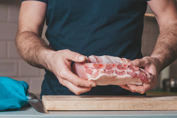 A man in the kitchen holds a large piece of meat - Foto, afbeelding