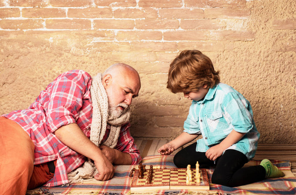 Grandfather and grandson playing chess. Grandfather and grandson are playing chess and smiling while spending time together at home. Chessman. - Foto, Imagen