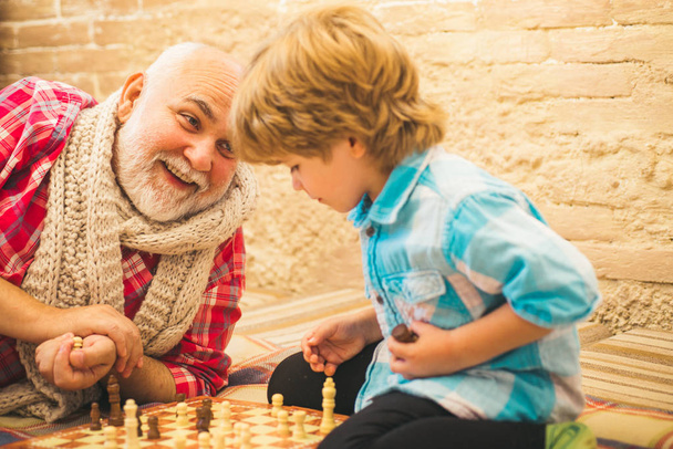 Διαγωνισμός σκακιού. Χαριτωμένο αγόρι αναπτύσσει στρατηγική σκακιού. Παππού και εγγονός παίζουν σκάκι. Παππούς και εγγονός έννοια. - Φωτογραφία, εικόνα