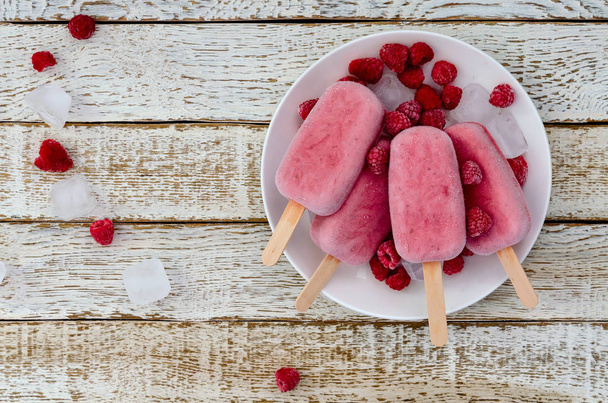 Strawberry and raspberry ice cream popsicles in white plate on white wooden background - Fotó, kép