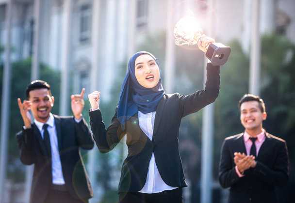 erfolgreiche muslimische Geschäftsfrau mit erhobenen Armen, die eine Trophäe in der Hand hält - Foto, Bild