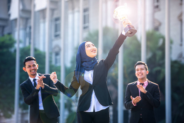 Exitosa mujer musulmana de negocios con los brazos en alto sosteniendo un trofeo a
 - Foto, imagen