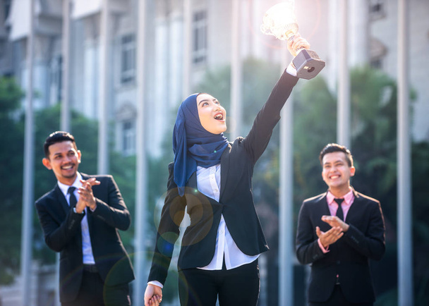 Femme d'affaires musulmane réussie avec les bras levés tenant un trophée a
 - Photo, image