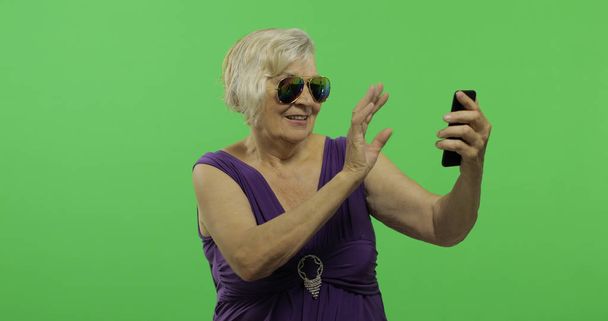 Μια ηλικιωμένη γυναίκα που έχει βίντεο chat χρησιμοποιώντας smartphone. Πλήκτρο αποχρώσεων - Φωτογραφία, εικόνα