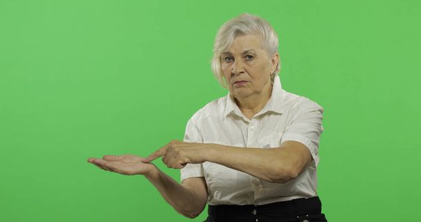 An elderly woman points at something and smiles. Old grandmother. Chroma key - Photo, Image