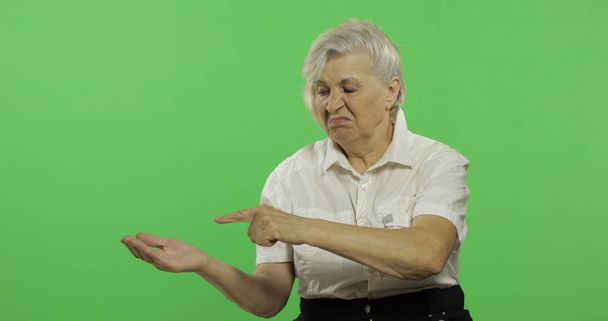 Yaşlı bir kadın bir şeyi işaret ediyor ve gülümsüyor. Yaşlı büyükanne. Chroma anahtarı - Fotoğraf, Görsel