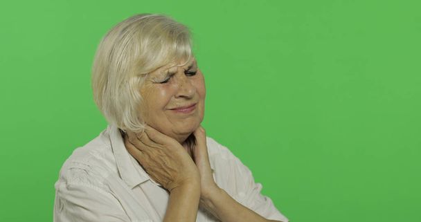 Μια ηλικιωμένη γυναίκα που έχει πόνο στο λαιμό. Η γριά γιαγιά. Πλήκτρο αποχρώσεων - Φωτογραφία, εικόνα